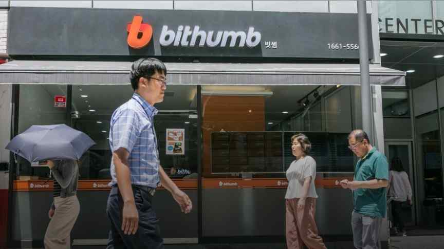 Korean man in checked shirt and glasses walking in front of Bithumb building