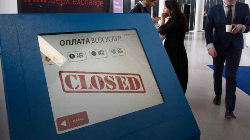 Blue Russian cryptocurrency ATM, screen shows CLOSED in red, business people walking in background