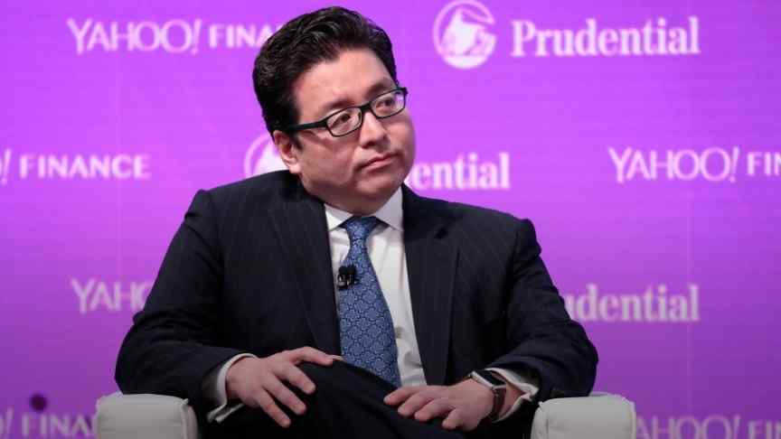 Tom Lee in dark suit, blue tie, sitting on purple background