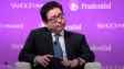 Tom Lee in dark suit, blue tie, sitting on purple background