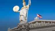 statue of a women with golden hat holding a pole and Ethereum coin on building of OeKB, Austrain flag in the back