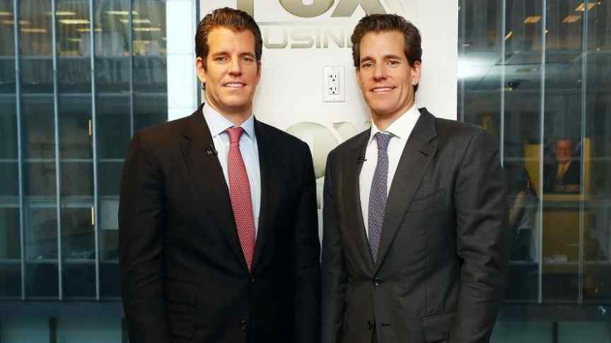 Winklevoss twins in suits, grey and red ties, standing in front of building