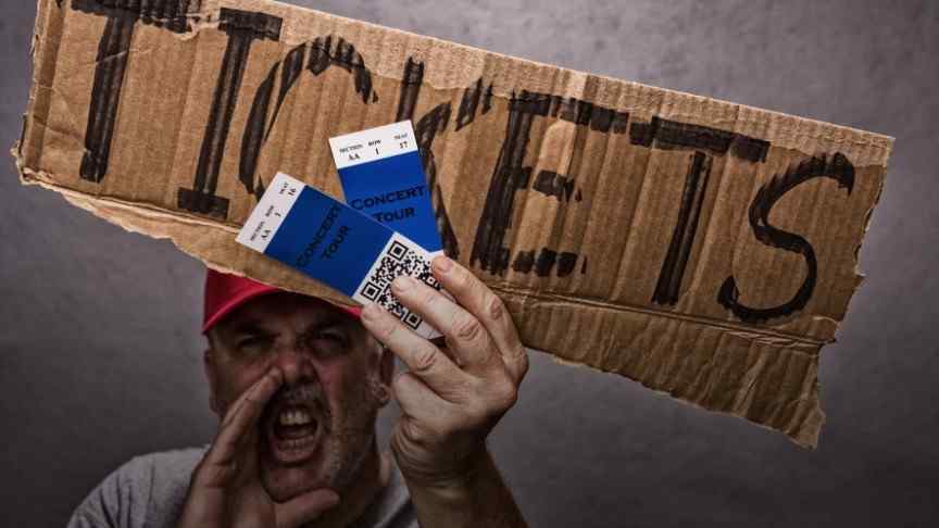 man in red hat shouting and holding cardboard sign saying TICKETS and two tickets