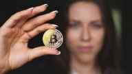 Picture of a woman showing a Bitcoin with the focus on the coin