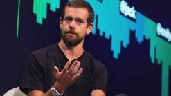 Jack Dorsey in black shirt with raised hand on background of black screen with green graph
