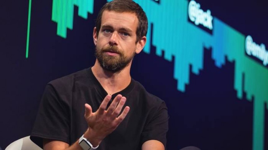 Jack Dorsey in black shirt with raised hand on background of black screen with green graph