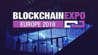 Sign: Blockchain written in white Expo written in Purple, Europe 2018 in white on purple bacground. In the Background lit conference room