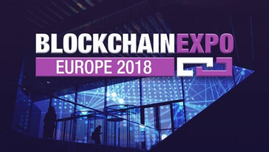 Sign: Blockchain written in white Expo written in Purple, Europe 2018 in white on purple bacground. In the Background lit conference room