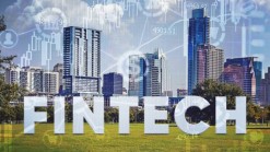 FINTECH written in white, on background of green lawn and skyscrapers, market graphs blurry in the background