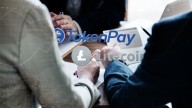 Token Pay and Litecoin names and logos, on background of businessmen in suits sitting around table holding documents