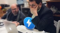 Nick Spanos in black suit sitting in front of Apple lap top, Zap logo in blue