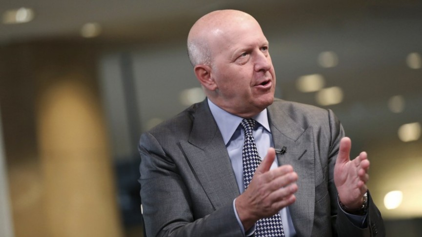 David Solomon in suit and tie mid-speech holding hands up