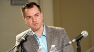 Austin Petersen in brown checkered jacket an dblue shirt, mid-speech, sitting next to two microphones