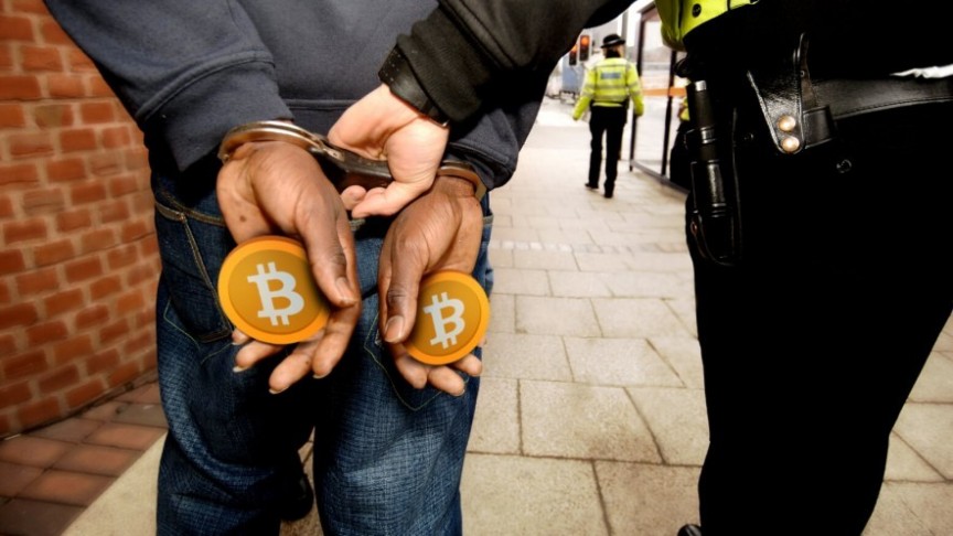 Man in handcuffs holding orange Bitcoins walking next to a police officer holding the cuffs, shot from behind