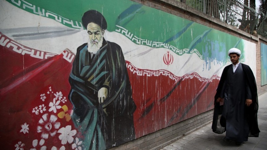 Iran's flag as a graffiti painting on wall, man walking in black robe 