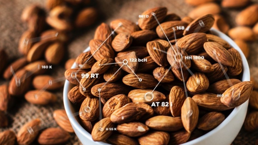 a white bowl filled with almonds, almonds scattered on the sides