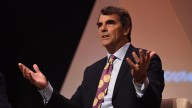 Tim Draper sitting with raised hands and suit and purple tie with Bitcoins 